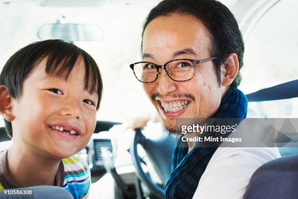 man wearing glasses and boy sitting in a car, smiling at camera. - asian smiling father son stock pictures, royalty-free photos & images