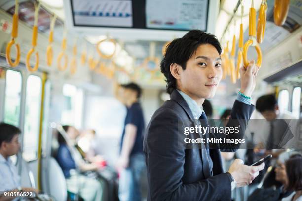 businessman wearing suit standing on a commuter train, holding mobile phone. - commuter train stock pictures, royalty-free photos & images