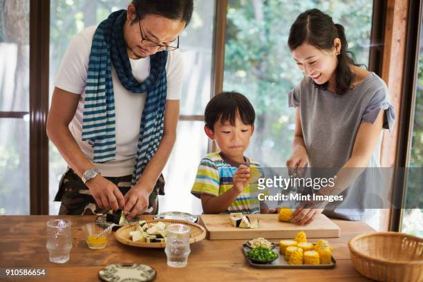 man, woman and boy standing at a table, preparing corn on the cob, smiling. - the japanese wife foto e immagini stock