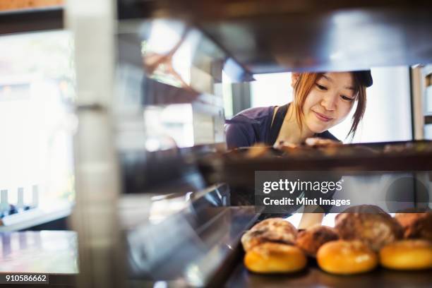 woman working in a bakery, placing large trays with freshly baked rolls on a trolley. - back to work stock-fotos und bilder