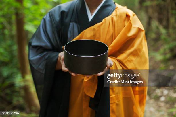 close up of buddhist monk wearing black and yellow robe, holding singing bowl. - shingon buddhismus stock-fotos und bilder