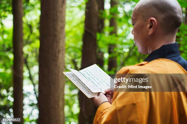 side view of buddhist monk with shaved head wearing black and yellow robe, standing outdoors, holding prayer text. - religiös text bildbanksfoton och bilder