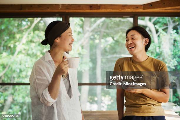 man and woman standing indoors, holding coffee mugs, looking at each other, smiling. - 30 39 jaar stockfoto's en -beelden