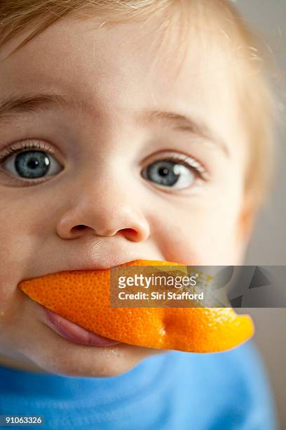 young boy with orange slice in mouth, portrait - siri stafford stock pictures, royalty-free photos & images