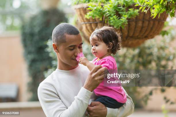 mixed race father holding baby girl smelling a flower - hanging basket stock pictures, royalty-free photos & images