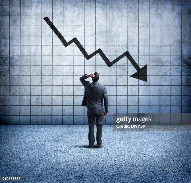 businessman looking up at downward trending arrow with concern - bankruptcy stock pictures, royalty-free photos & images