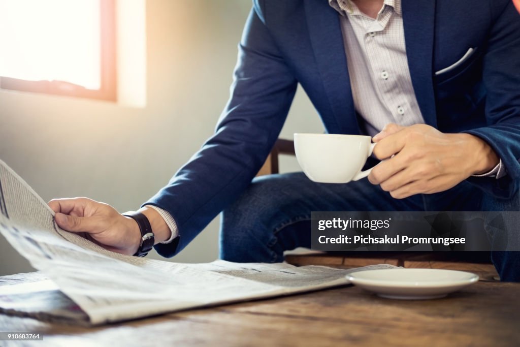 Midsection Of Businessman Holding Coffee While Reading Newspaper On Table