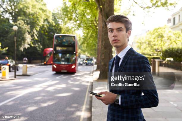 young businessman standing in the street holding smartphone - man check suit stock pictures, royalty-free photos & images