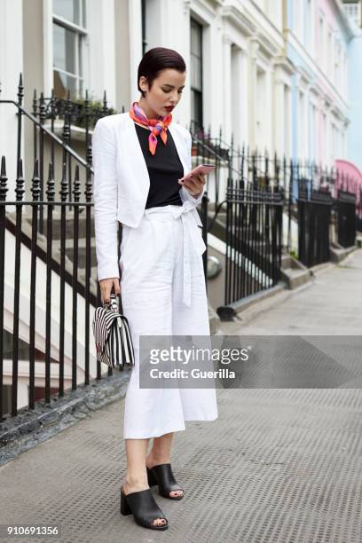 woman in linen suit looking at phone in street, full length - woman scarf trousers stockfoto's en -beelden