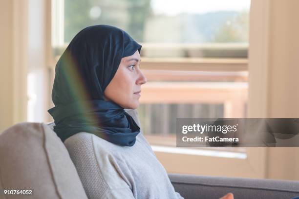 arabische-amerikaanse vrouw zitten rustig in haar woonkamer - woman in a shawl stockfoto's en -beelden