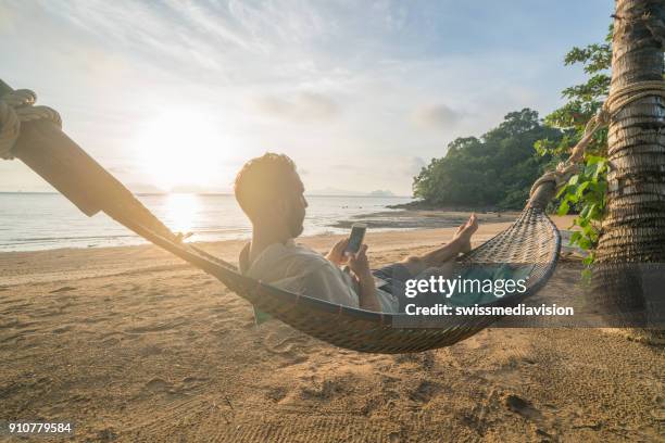man on hammock using mobile phone, thailand - hammock imagens e fotografias de stock