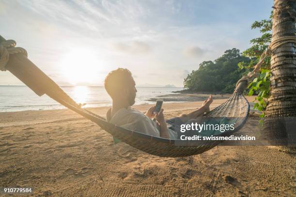 homem na rede usando telefone celular, tailândia - homem costas - fotografias e filmes do acervo