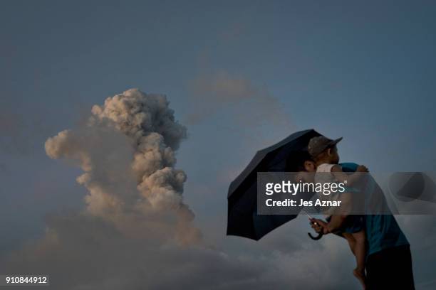 Boys take cover with an umbrela as Mayon spews ash and lava on January 26 in Albay, Philippines. Over 70,000 villagers have been evacuated and camped...
