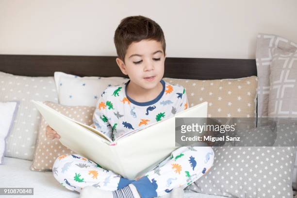a little boy reading book on the bed - moving down to seated position stock pictures, royalty-free photos & images