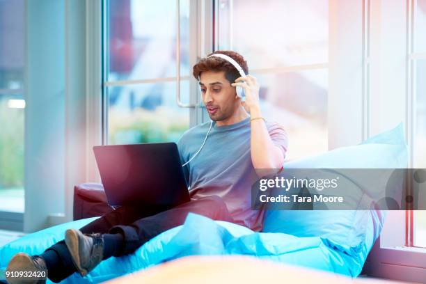 young man relaxing with headphones and laptop - bean bags fotografías e imágenes de stock
