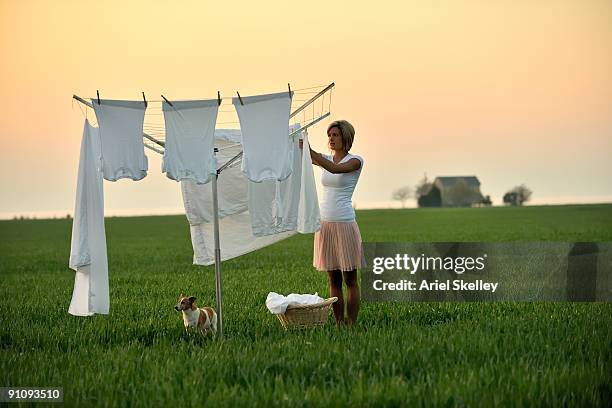 young woman doing laundry in field at sunrise - wäschespinne stock-fotos und bilder