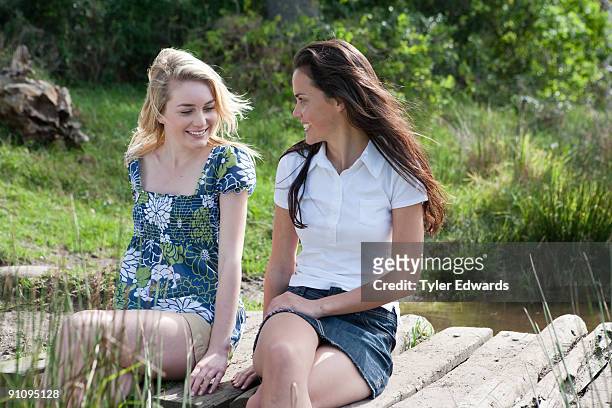two woman sitting on wooden bridge - moving down to seated position stock pictures, royalty-free photos & images
