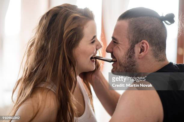 joyous young couple eating chocolate together - bijten stockfoto's en -beelden
