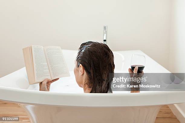 woman in bath reading with glass of wine - woman bath tub wet hair stock pictures, royalty-free photos & images