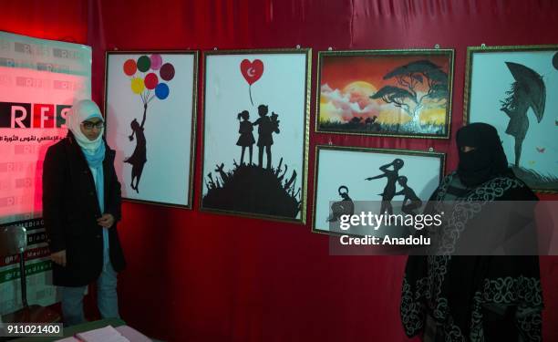 People inspect the paintings of Syrian painters Fatima Ahmed and Hikmet Ismael during an art exhibition which is on Syrian people's experience,...