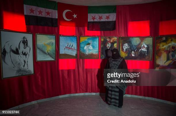 People inspect the paintings of Syrian painters Fatima Ahmed and Hikmet Ismael during an art exhibition which is on Syrian people's experience,...