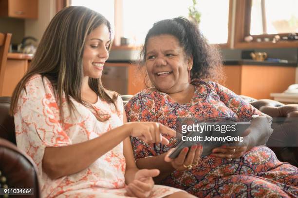 two women using digital tablet smiling and laughing - minority groups stock pictures, royalty-free photos & images