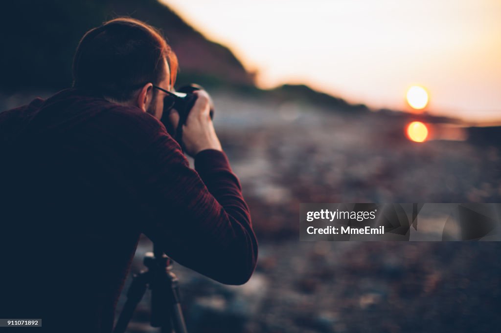 Joven sosteniendo una cámara sobre un trípode y tomar una fotografía del mar. Gaspesie, Quebec, Canadá