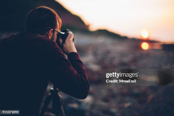 young man holding a camera on a tripod and taking a picture of the sea. gaspesie, quebec, canada - gaspe peninsula stock pictures, royalty-free photos & images