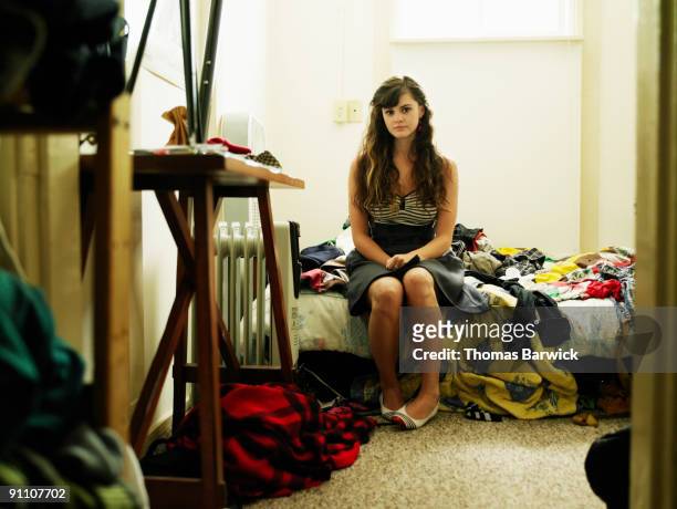 portrait young woman sitting on bed in bedroom - scruffy stock-fotos und bilder