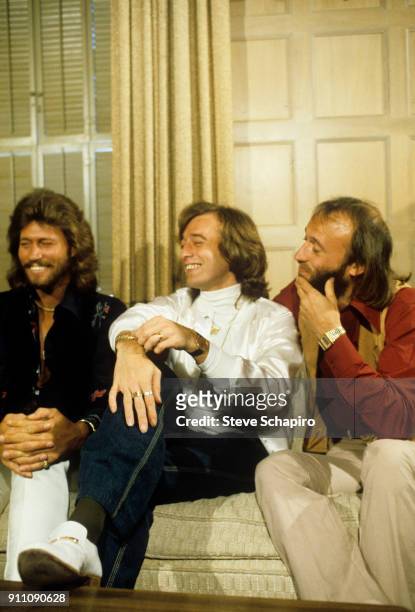 View of the pop group the Bee Gees, from left, Barry Gibb, Robin Gibb , and Maurice Gibb , as they share a laugh, seated on a couch, 1970s.