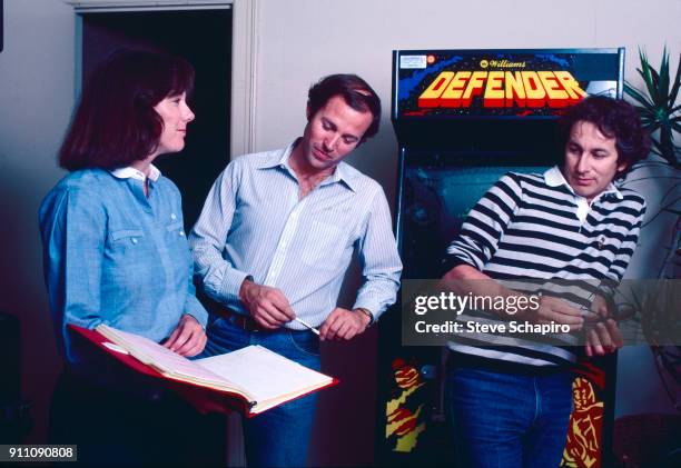 View of, from left, American film producers Kathleen Kennedy and Frank Marshall, and film director Steven Spielberg, who leans on an Defender arcade...