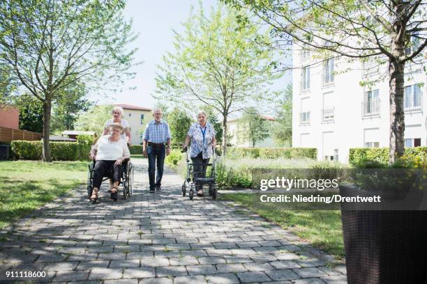 senior man and women with mobility walker and wheelchair at garden footpath - rentnersiedlung stock-fotos und bilder