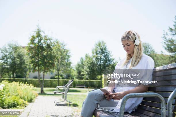 female doctor listening to music with smart phone and headphones at garden - doctor using smartphone stock-fotos und bilder