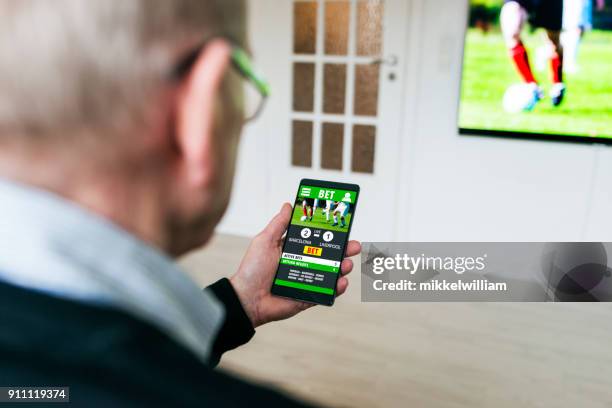 hombre las apuestas en juego de futbol con las apuestas de la aplicación en el teléfono en casa - gambling fotografías e imágenes de stock