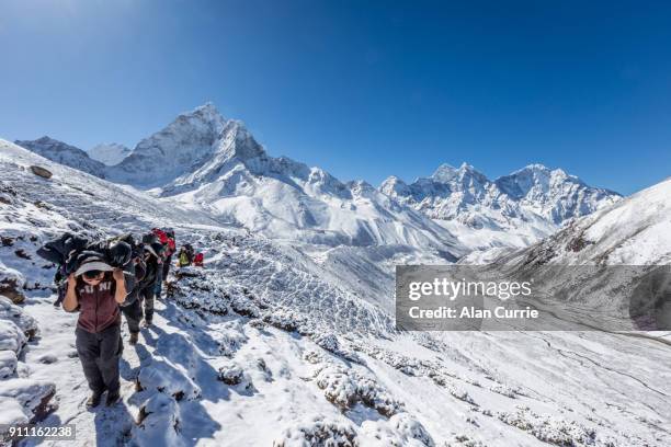 sherpas und träger mit gepäck im schnee gefüllt bergen von nepal - mt everest base camp stock-fotos und bilder