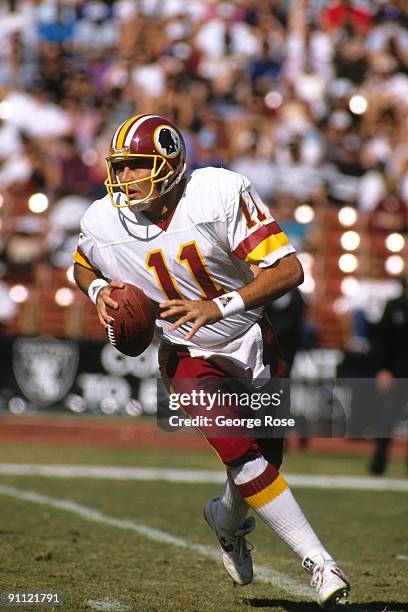 Quarterback Mark Rypien of the Washington Redskins scrambles with the ball during the game against the Los Angeles Raiders at RFK Stadium on October...