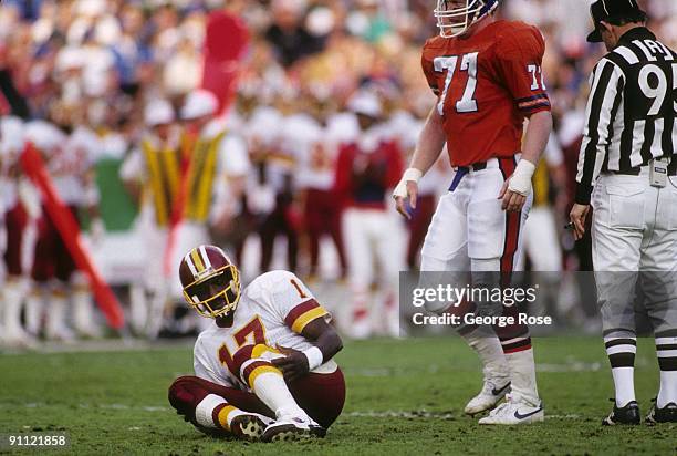 Quarterback Doug Williams of the Washington Redskins goes down in pain in front of defensive end Karl Mecklenburg of the Denver Broncos during Super...