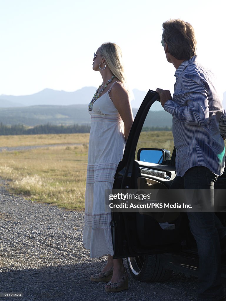 Well-dressed couple park on gravel road, mtns