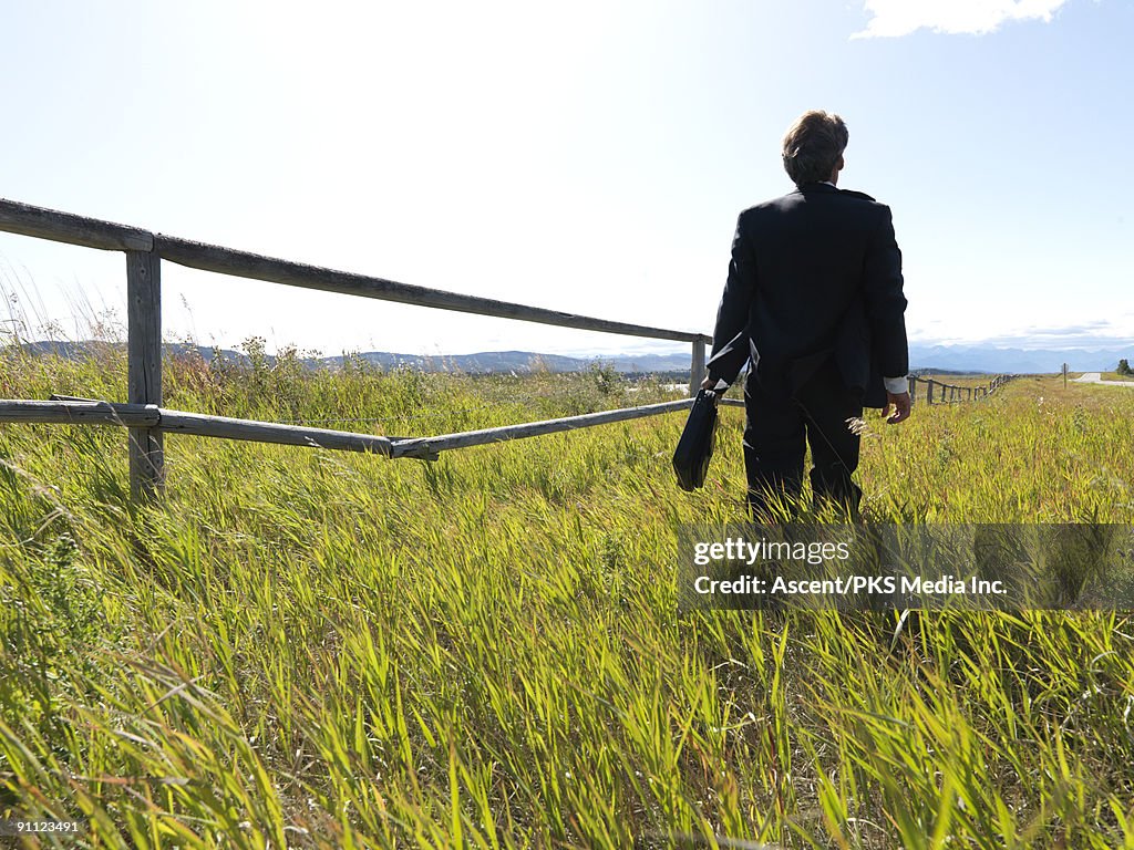 Businessman walks through grasses alongside fence