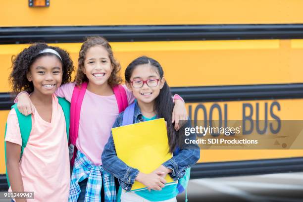 elementary age female friends in front of school bus - school bus kids stock pictures, royalty-free photos & images