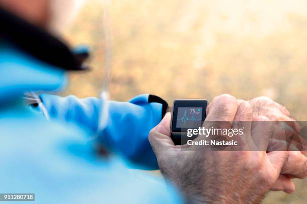 elderly man using smart watch measuring heart rate - computador utilizável como acessório imagens e fotografias de stock
