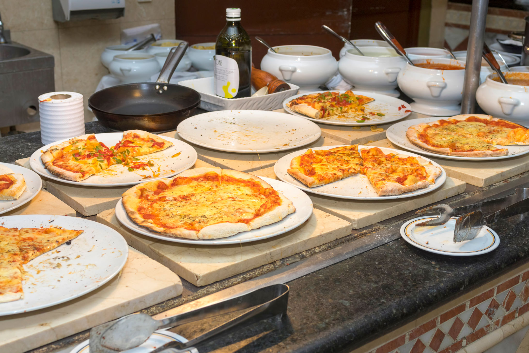 Different kinds of pizza on white plates on a buffet Different kinds of pizza on white plates on a buffet