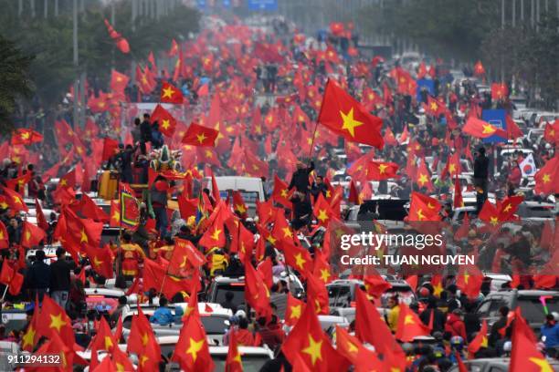 Large crowd of football fans wave the national flag as they follow a bus carrying the members of the U-23 Vietnamese National team through the...