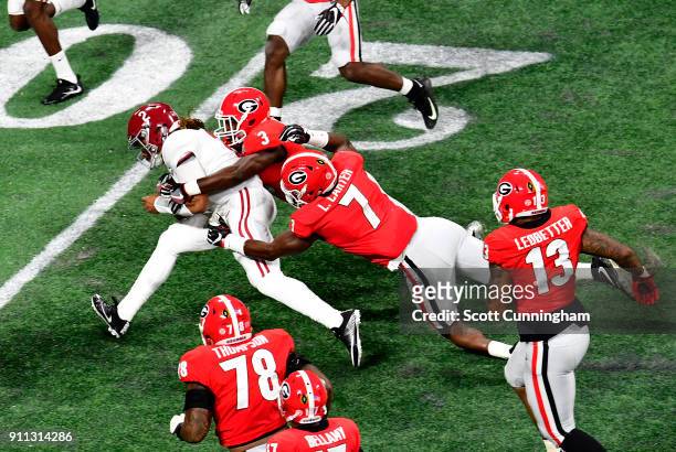 Jalen Hurts of the Alabama Crimson Tide is tackled by Lorenzo Carter and Roquan Smith of the Georgia Bulldogs in the CFP National Championship...