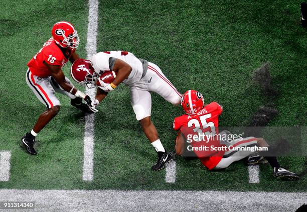 Damien Harris of the Alabama Crimson Tide carries the ball against Aaron Davis and Deandre Baker of the Georgia Bulldogs in the CFP National...