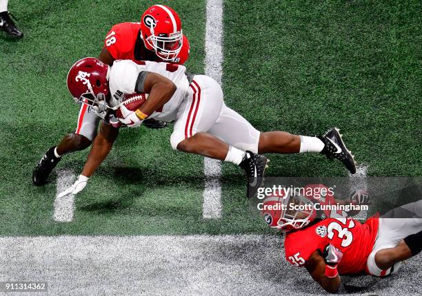 Damien Harris of the Alabama Crimson Tide carries the ball against Aaron Davis and Deandre Baker of the Georgia Bulldogs in the CFP National...