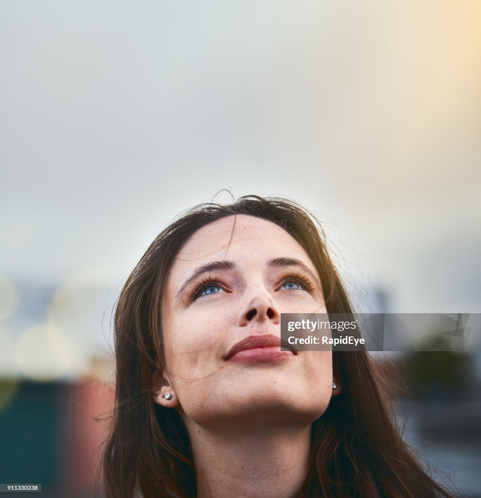 Junge Frau schaut hoffnungsvoll, wie sie ihre Augen in den Himmel hebt