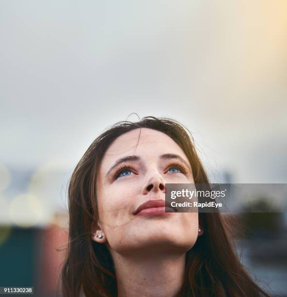 young woman looks hopeful as she raises her eyes towards the sky - people looking stock pictures, royalty-free photos & images