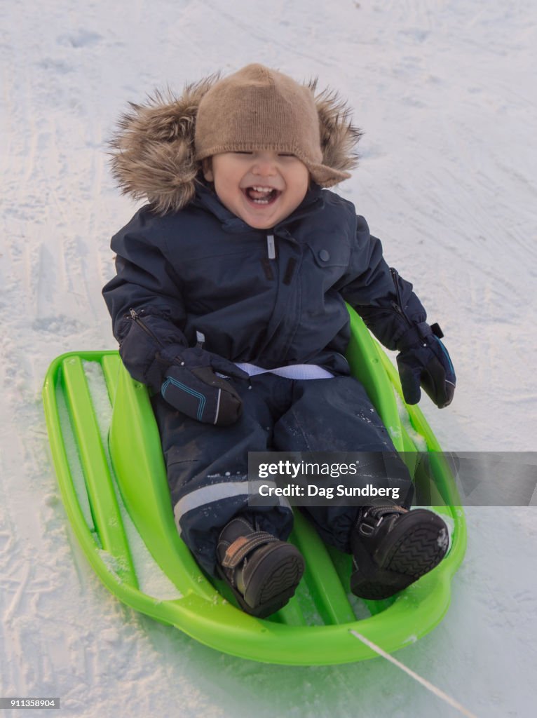 Toddler riding on green baby sled