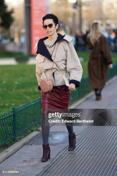 Guest wears sunglasses, a beige coat, a red leather skirt, a pink chanel circular bag, gray tights, shoes, outside Chanel, during Paris Fashion Week...